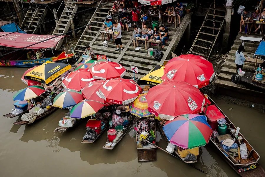 Barcas de comida con sombrillas rojas amarradas junto a las escaleras del canal del mercado flotante de Amphawa