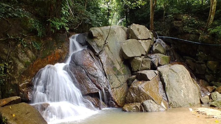 Agua cayendo entre rocas y vegetación en la Cascada de Kathu