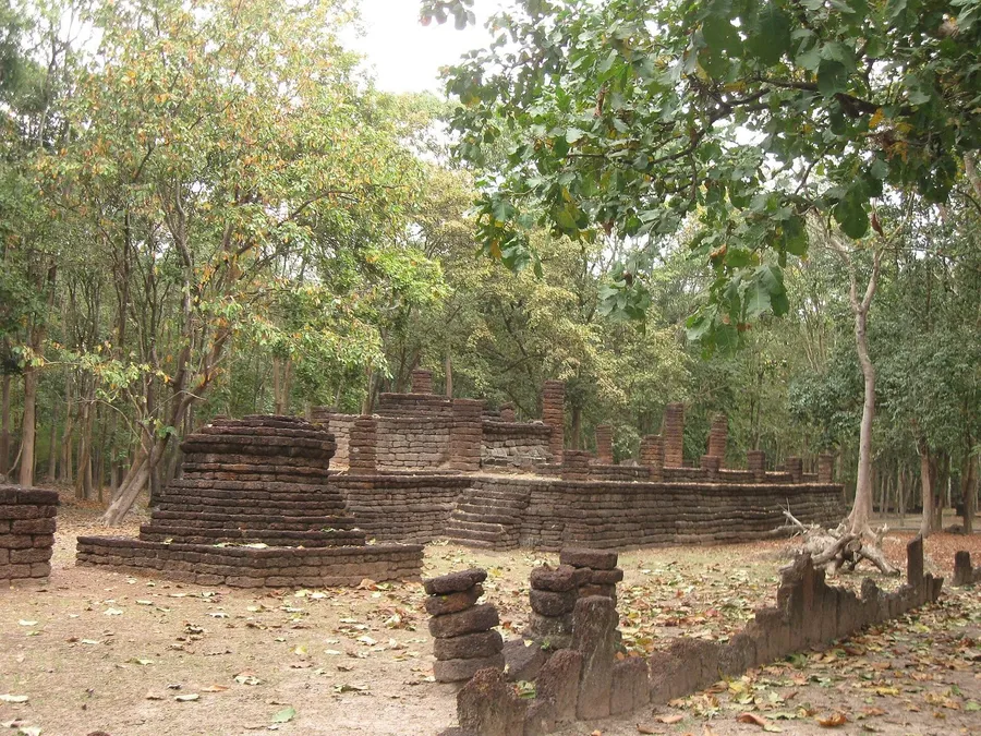 Ruinas de laterita rojiza del Wat Kamphaeng Ngam: base de chedi y columnas entre el bosque del parque histórico