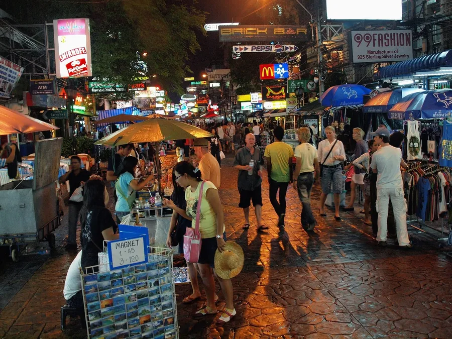 Khao San Road de noche: calle peatonal llena de puestos, letreros de neón y viajeros paseando en Bangkok.