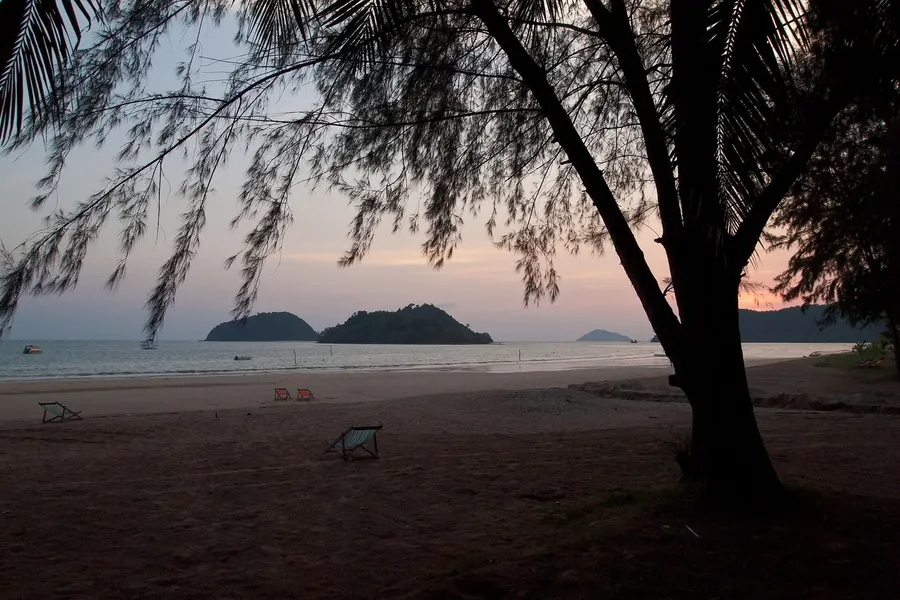 Atardecer en una playa vacía de Koh Mak, con tumbonas en la arena e islotes verdes al fondo