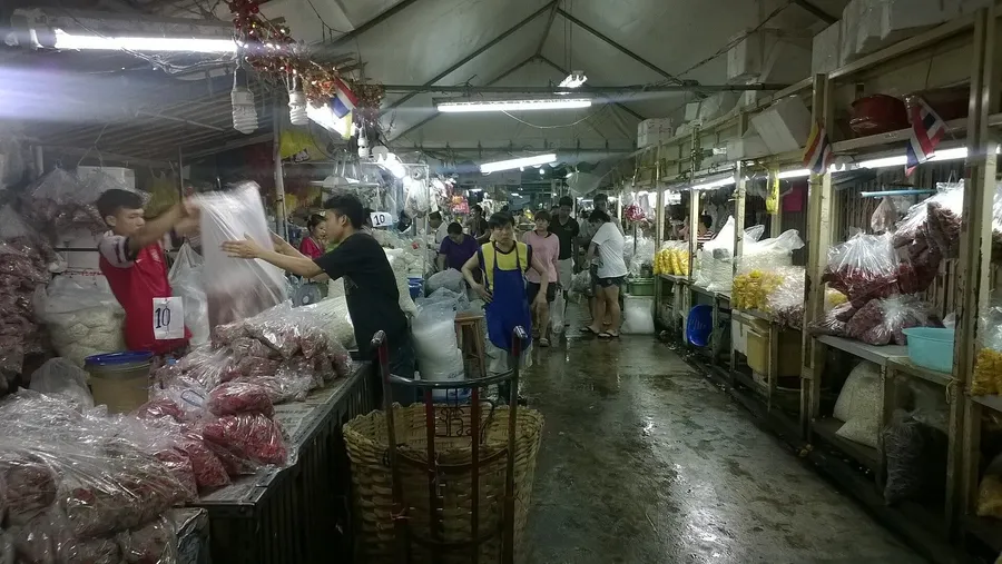 Pasillo del mercado de flores Pak Khlong Talat, con puestos y sacos de flores envueltas en plástico