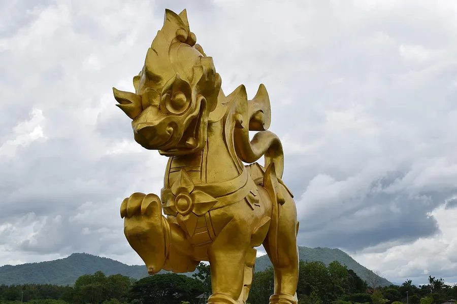 Campos verdes y estatua dorada del león en Singha Park Chiang Rai