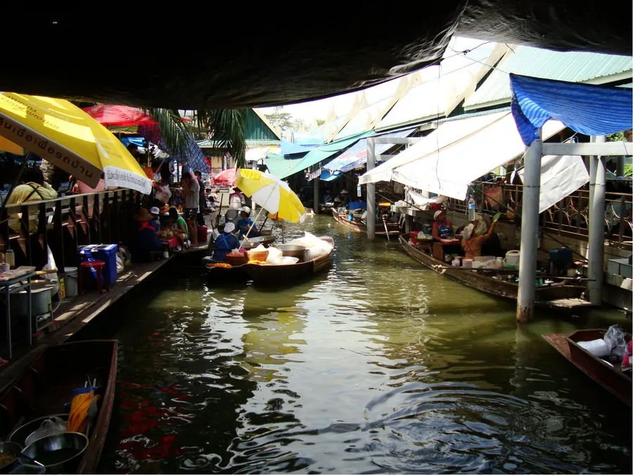Barcas de comida amarradas en el canal del mercado flotante de Taling Chan, bajo toldos y sombrillas de colores