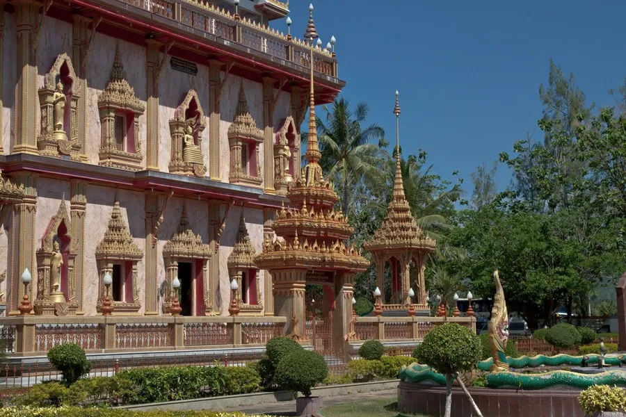 Chedi de Wat Chalong, Phuket: fachada con hornacinas de budas dorados, pabellones con agujas y naga