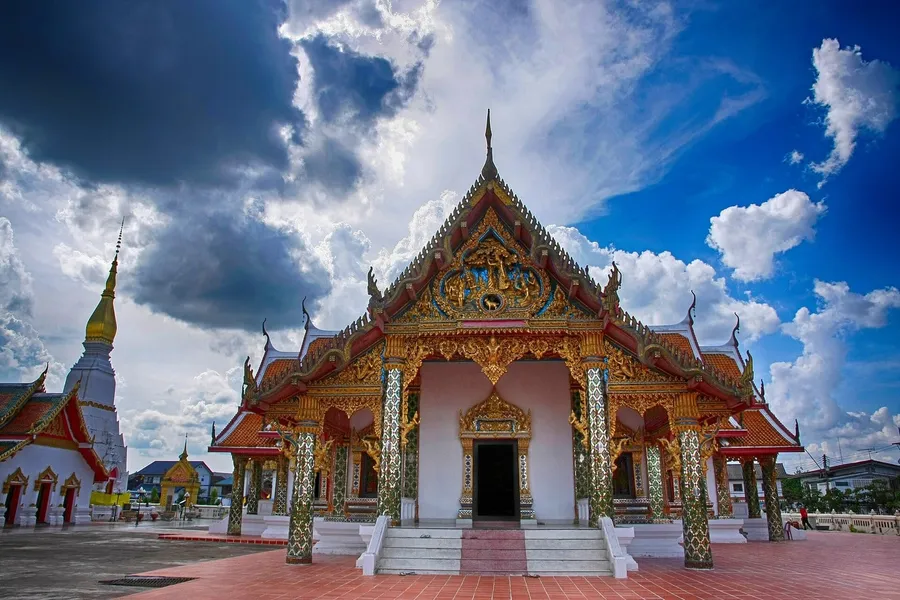 Ubosot dorado de Wat Phra That Choeng Chum en Sakon Nakhon, con la estupa blanca de estilo lao al fondo a la izquierda