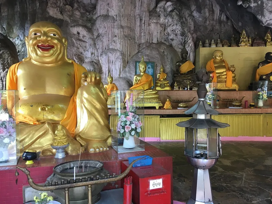 Buda dorado sonriente y estatuas de Buda bajo la roca caliza de la cueva de Wat Tham Suea, en Krabi.